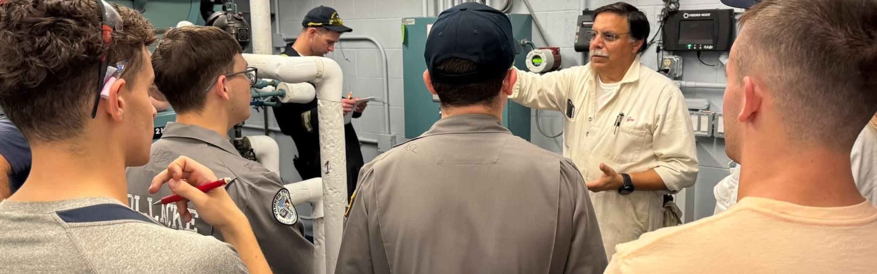 Man in boiler suit instructs students in a steam lab