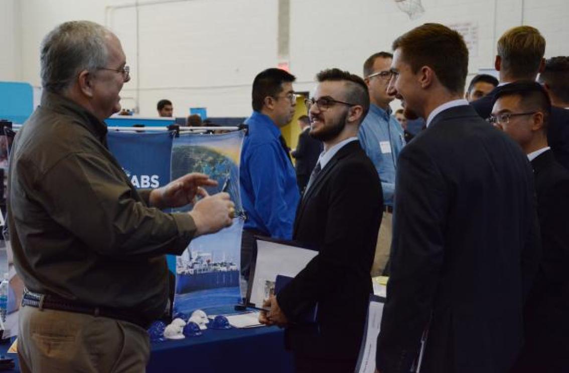 A couple students talk at a Career Fair stand with a potential employer.