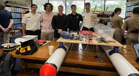 Five students standing behind a homemade pontoon boat sitting on a table