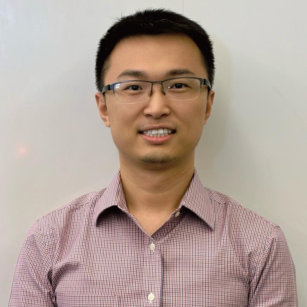 A man with black hair and glasses looks at the camera